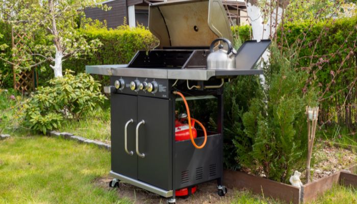 Outdoor gas grill with connected propane tank in backyard near greenery