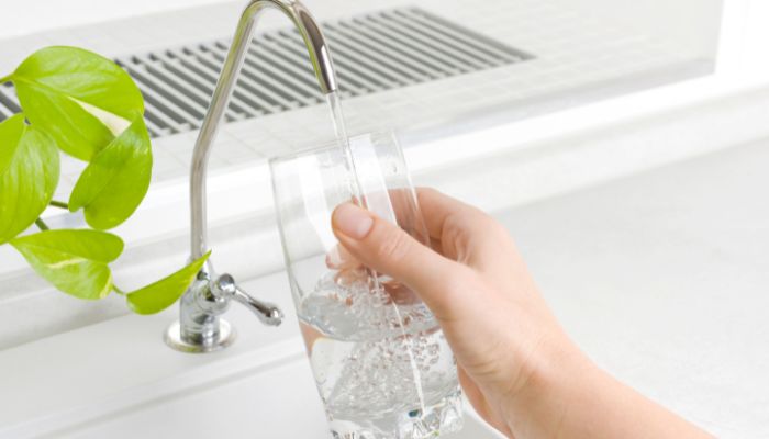 Hand filling a glass of clean, filtered water from a modern kitchen faucet.